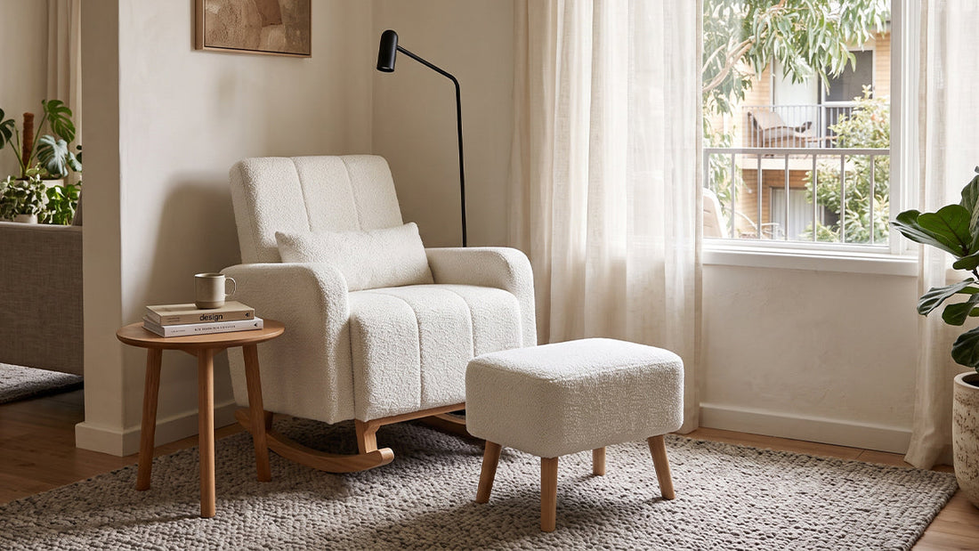 Cream bouclé rocking chair with a matching ottoman and lumbar cushion next to a wooden side table in a sunlit living room.