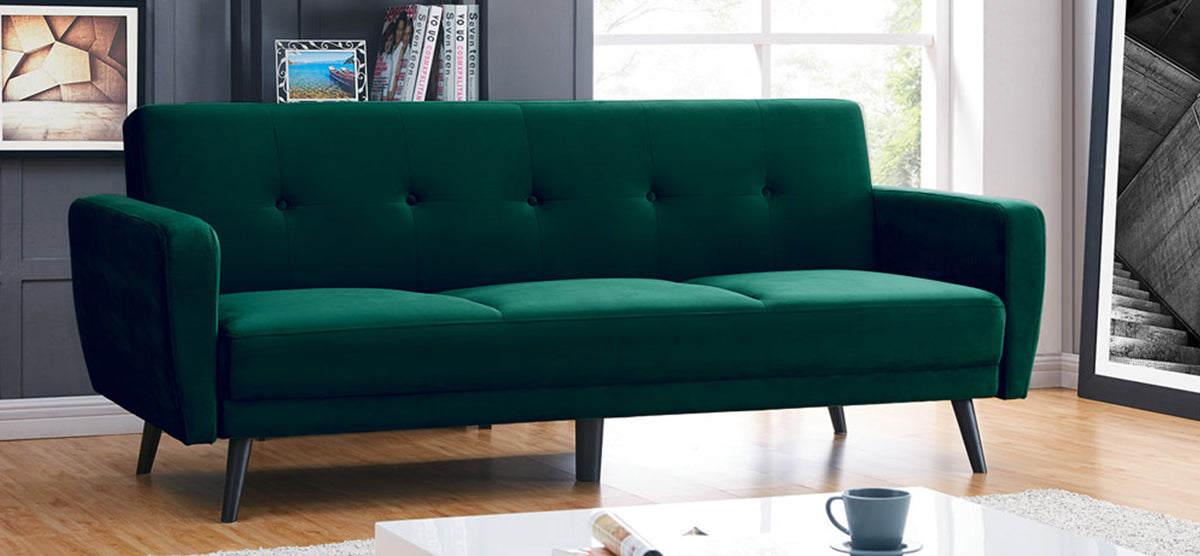 Modern living room with a deep green, mid-century sofa featuring tufted back cushions and tapered wooden legs, paired with a white coffee table holding an open magazine and ceramic mug.