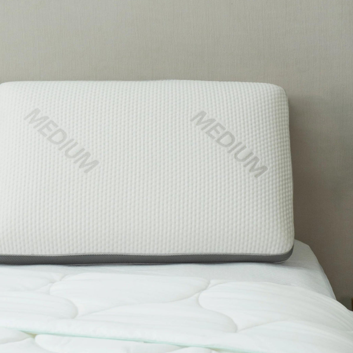 Signature memory foam pillow, Medium, with grey gusset trim, resting on a bed against a headboard