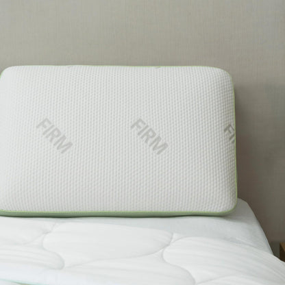 Signature memory foam pillow, Firm, with green gusset trim, resting on a bed against a headboard