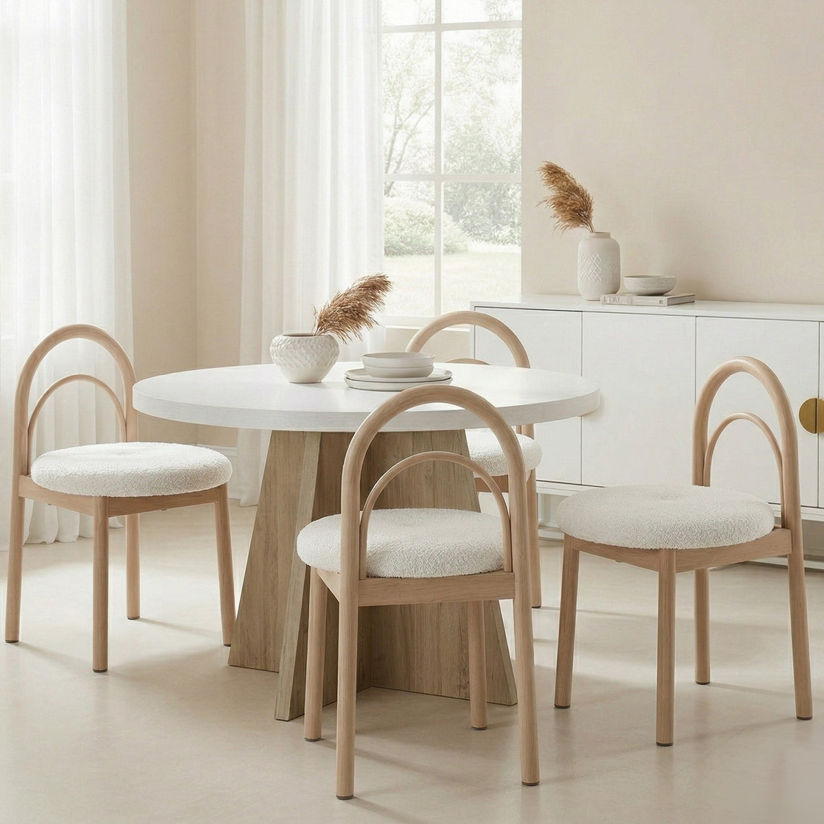 Modern round white dining table with a wooden base, surrounded by four light wood dining chairs with arched backs and white textured seats.