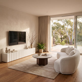 White bouclé curved sofa paired with a round coffee table and a white TV unit in a bright, modern living room opening to an outdoor deck.