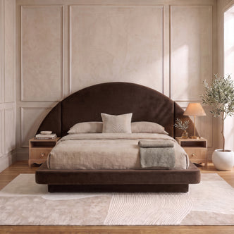 A modern neutral bedroom showcasing a dark brown velvet bed frame with an oversized half-moon headboard, styled with beige bedding and wooden nightstands on a textured abstract rug.