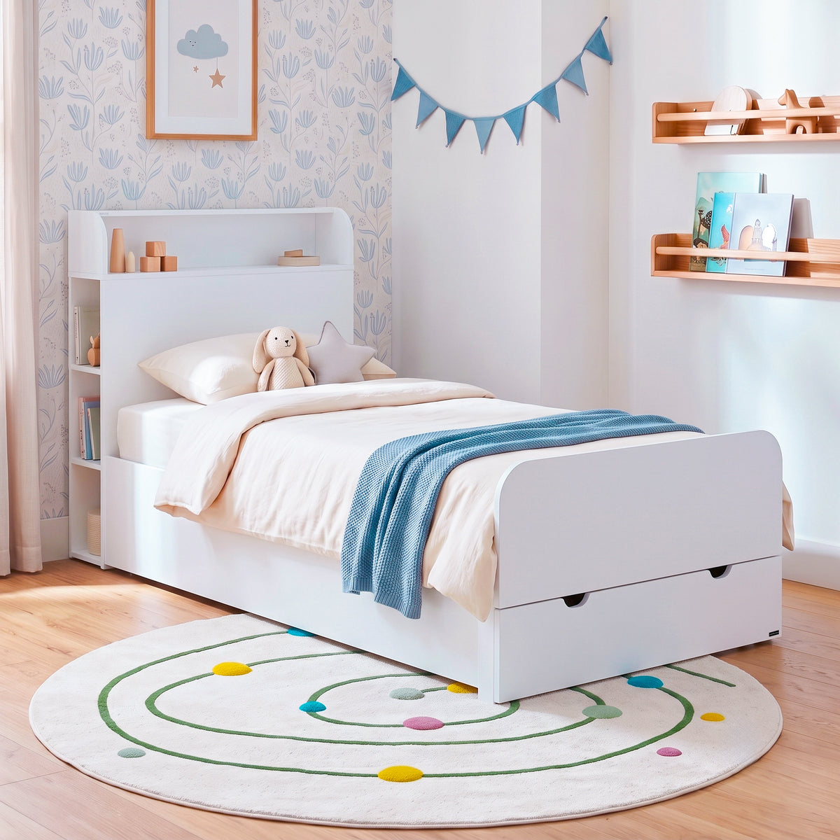 White children's bed with shelf headboard and pull-out drawer in a decorated bedroom.