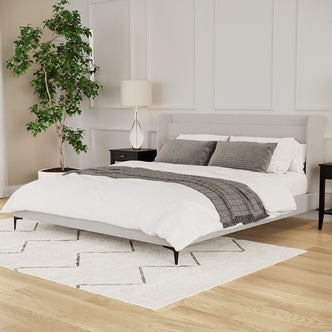 Beige boucle king bed frame with winged headboard, black legs, styled with white bedding and grey throw