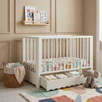 White timber baby cot with scalloped under-bed storage drawer, shown in nursery with patterned bedding