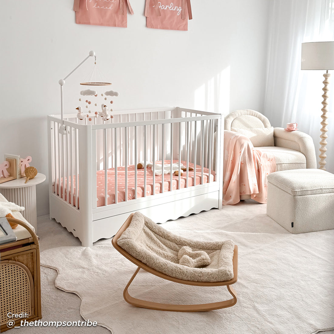 White timber baby cot with scalloped under-bed storage drawer, shown in nursery with pink bedding and matching mobile arm