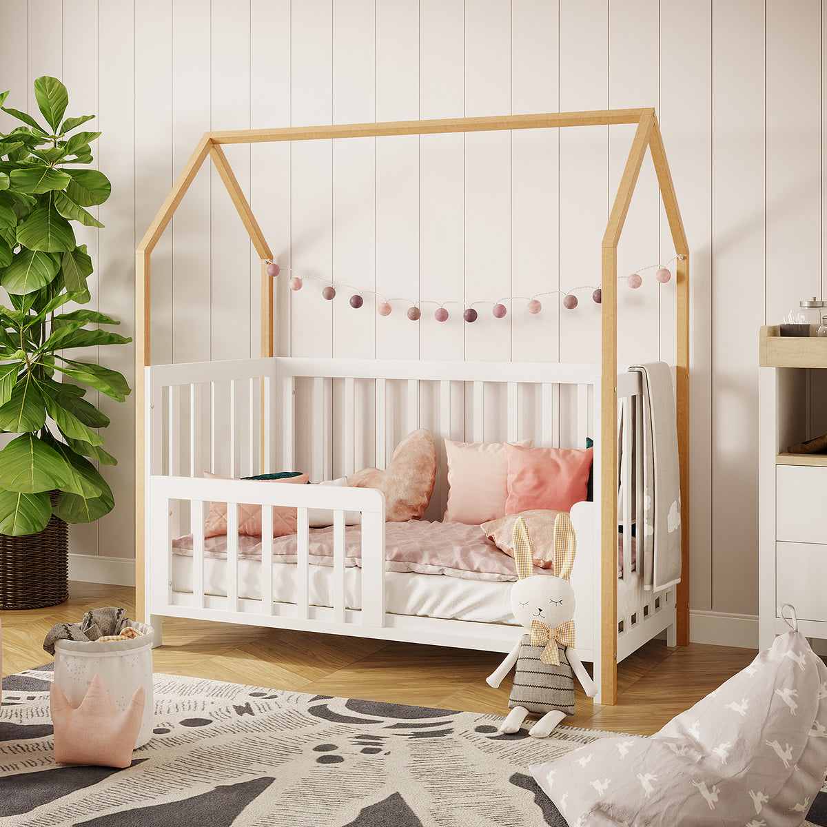 Damaris & Giro Baby Cot & Toddler Bed Kit Set in White features a house-frame design with a string of felt ball lights, pastel bedding, and a plush bunny, nestled in a cozy nursery corner.