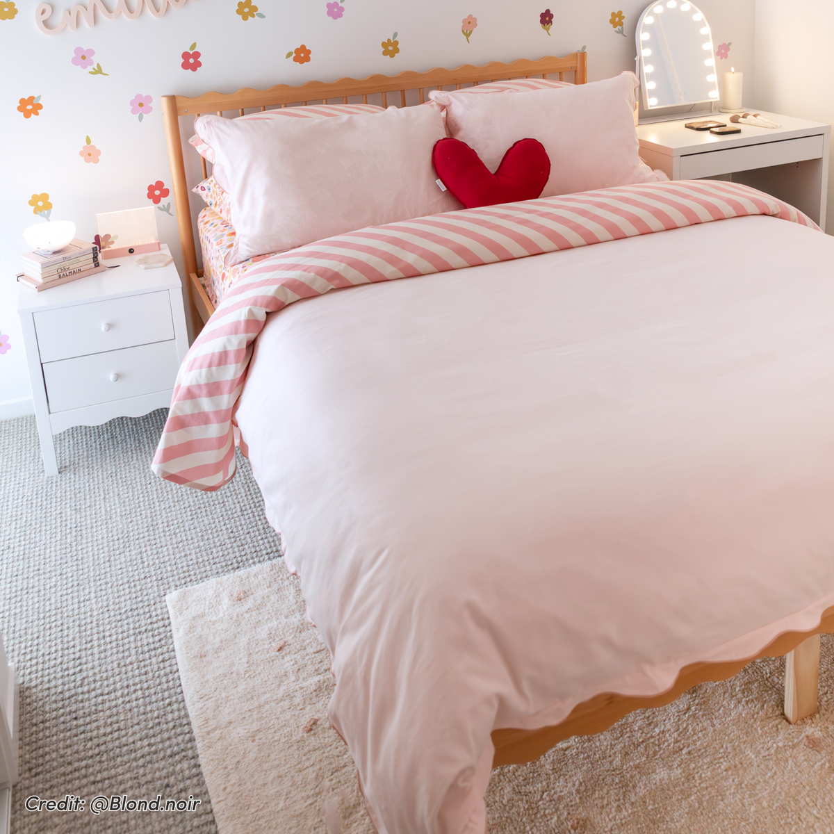 Natural hardwood scalloped double bed frame with pink and white striped bedding, red heart cushion, and curved headboard in a