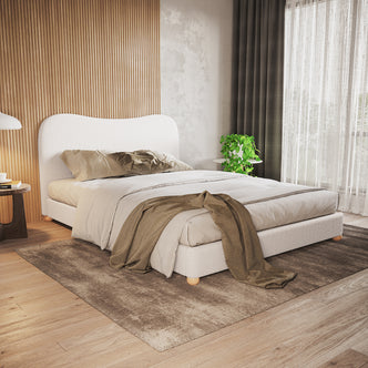 Ginnie Bouclé Curved Queen Bed Frame - Cream White showcased in a contemporary bedroom with a curved headboard, neutral bedding, light wood slat accent wall, and a plush brown area rug.