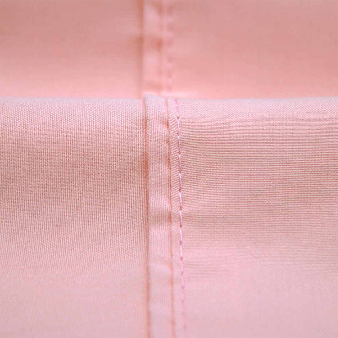 Close-up of blush pink bed sheet showing stitched seam and fabric texture