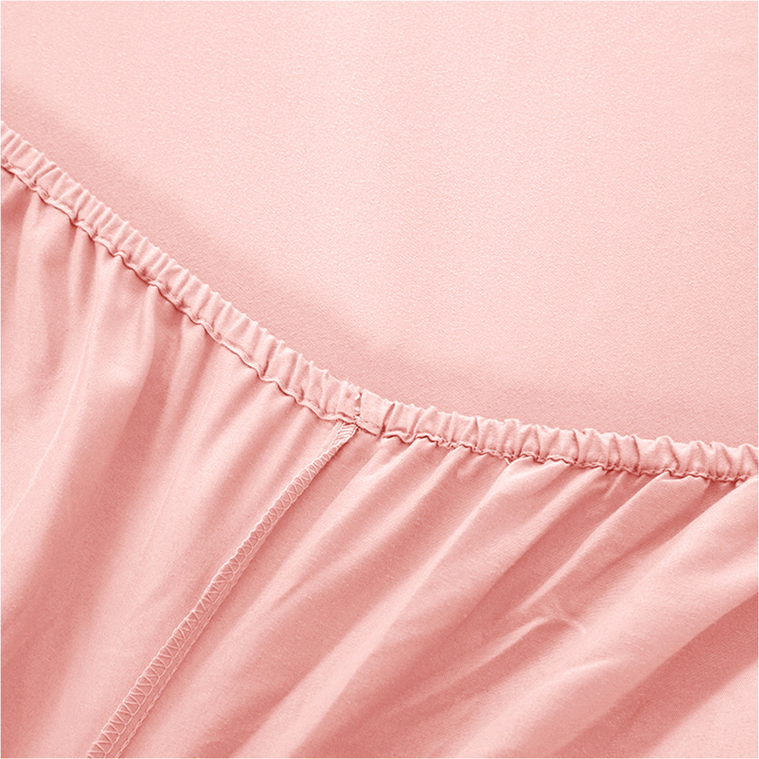 Close-up of blush pink fitted sheet with elastic edge and stitching detail