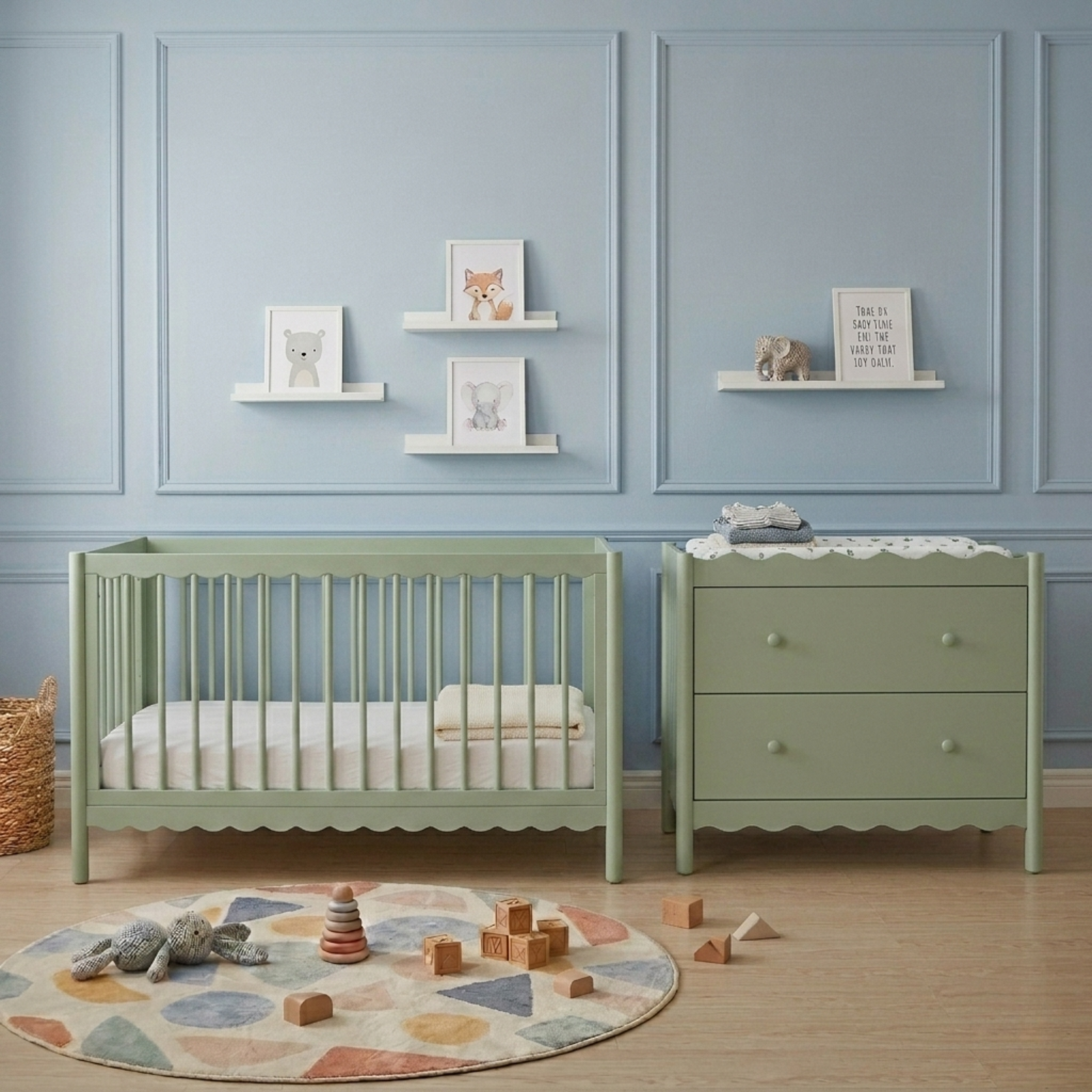 Sage green baby cot with scalloped base beside matching chest of drawers in blue nursery