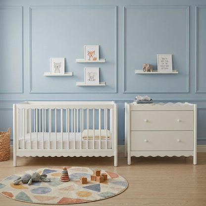 White wooden baby cot with scalloped edges beside matching chest of drawers in blue nursery