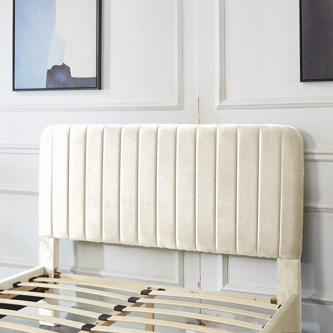 Seneca Double Upholstered Velvet Bed – Sandy White, featuring a vertically-channeled cream headboard, wooden slats for support, and minimalist paintings above, partially assembled against a paneled wall for a sophisticated look.
