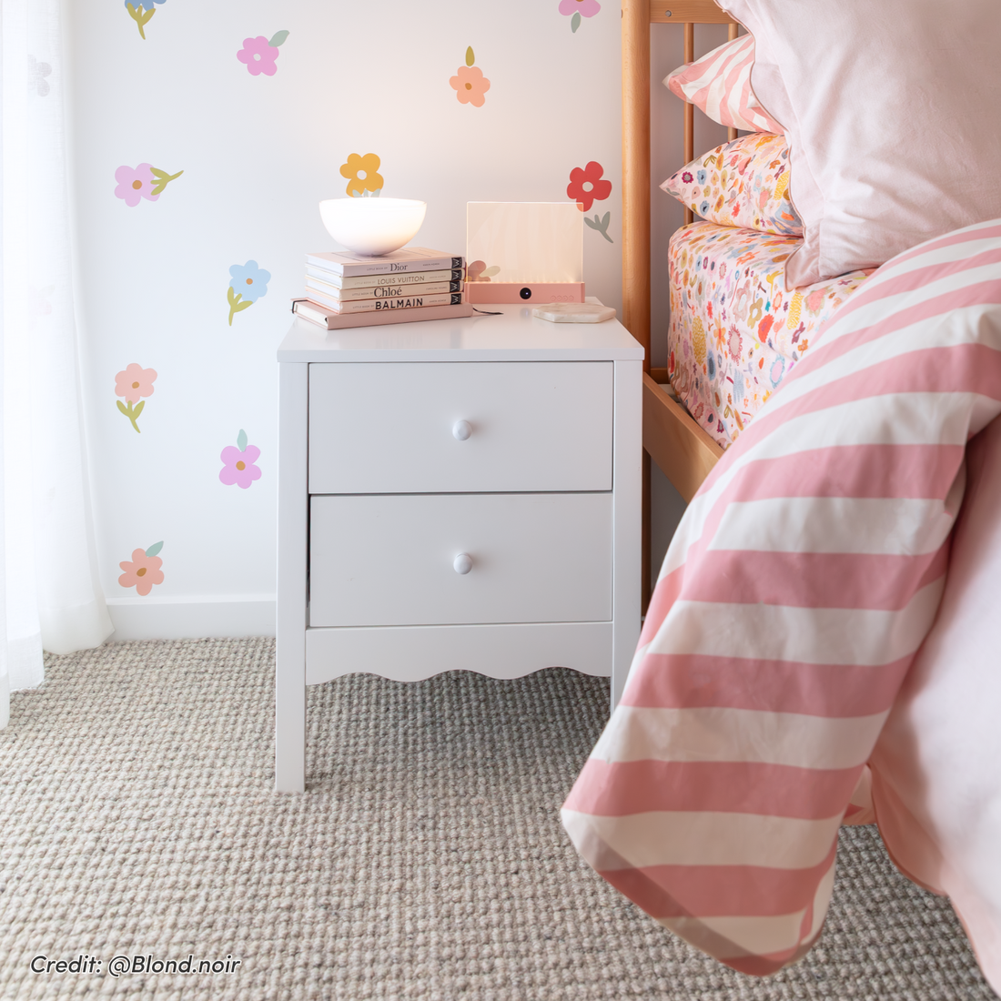 White two-drawer bedside table with round knobs and scalloped base, styled next to a bed with striped bedding
