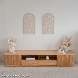 Eddie 200cm Hardwood Oak TV Entertainment Unit in Natural featuring a minimalist design with two central open cubbies, drawers at each end, and decorative dried florals on top.