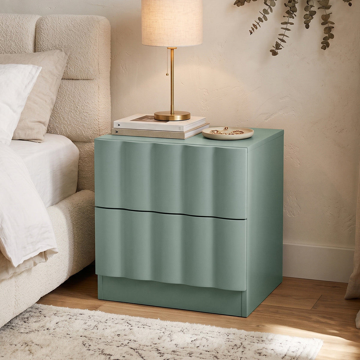 Hamish 2 Drawer Fluted Bedside Table in Sage with curved fluted front, displayed beside bed with lamp, books and phone on top