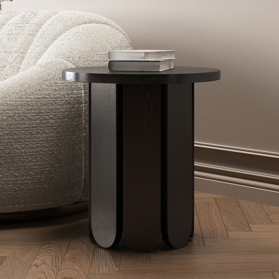 Hugo 45cm Round Side Table with Curve Detail in Black, showcasing a rounded top and sculptural base against a textured sofa, with two books on top, on a warm herringbone floor.
