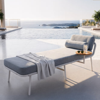 Andre Wicker Outdoor Sun Lounger Set of 2 in Light Grey beside an infinity pool, featuring a sleek white frame, light grey cushion, small wooden side table with iced water, and ocean view.