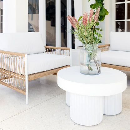 Basalt 70cm Indoor & Outdoor Concrete Coffee Table in White set in a minimalist outdoor area, featuring a round white tabletop with a glass vase, two woven lounge chairs, and a light patio floor.