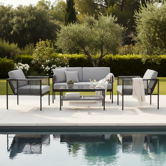 Brujas 4 Seater Wicker Outdoor Lounge Set in Grey beside a swimming pool with landscaped garden backdrop