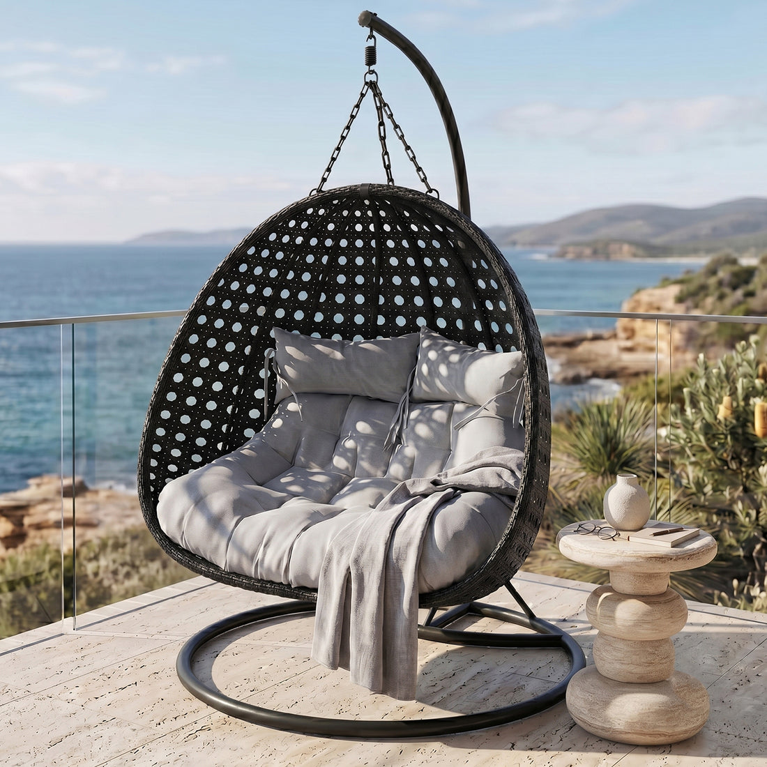 Buena 2-Seater Hanging Egg Chair in Black with grey cushions and throw, featuring a perforated rattan-style shell, chain