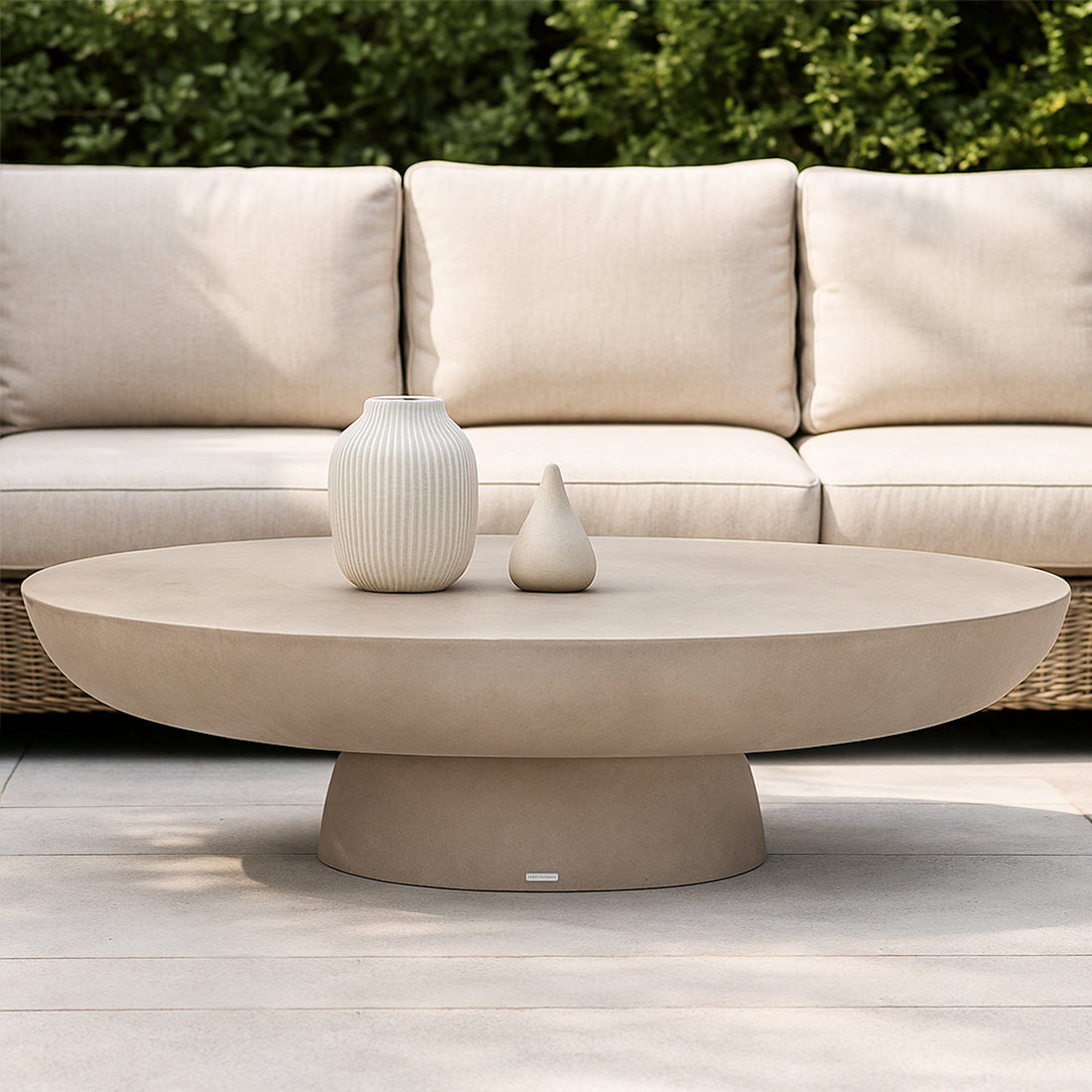 Cassius oval outdoor concrete coffee table in ivory with rounded base, displayed with two ceramic vases on light paving