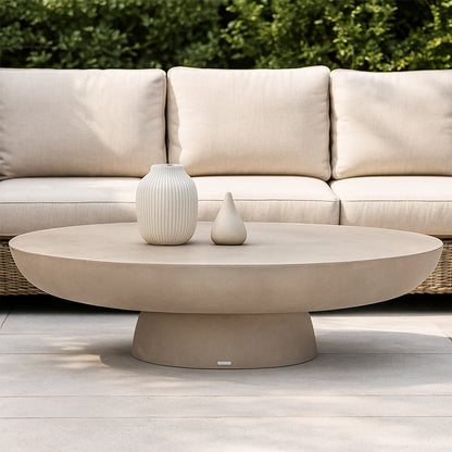 Cassius oval outdoor concrete coffee table in ivory with rounded base, displayed with two ceramic vases on light paving