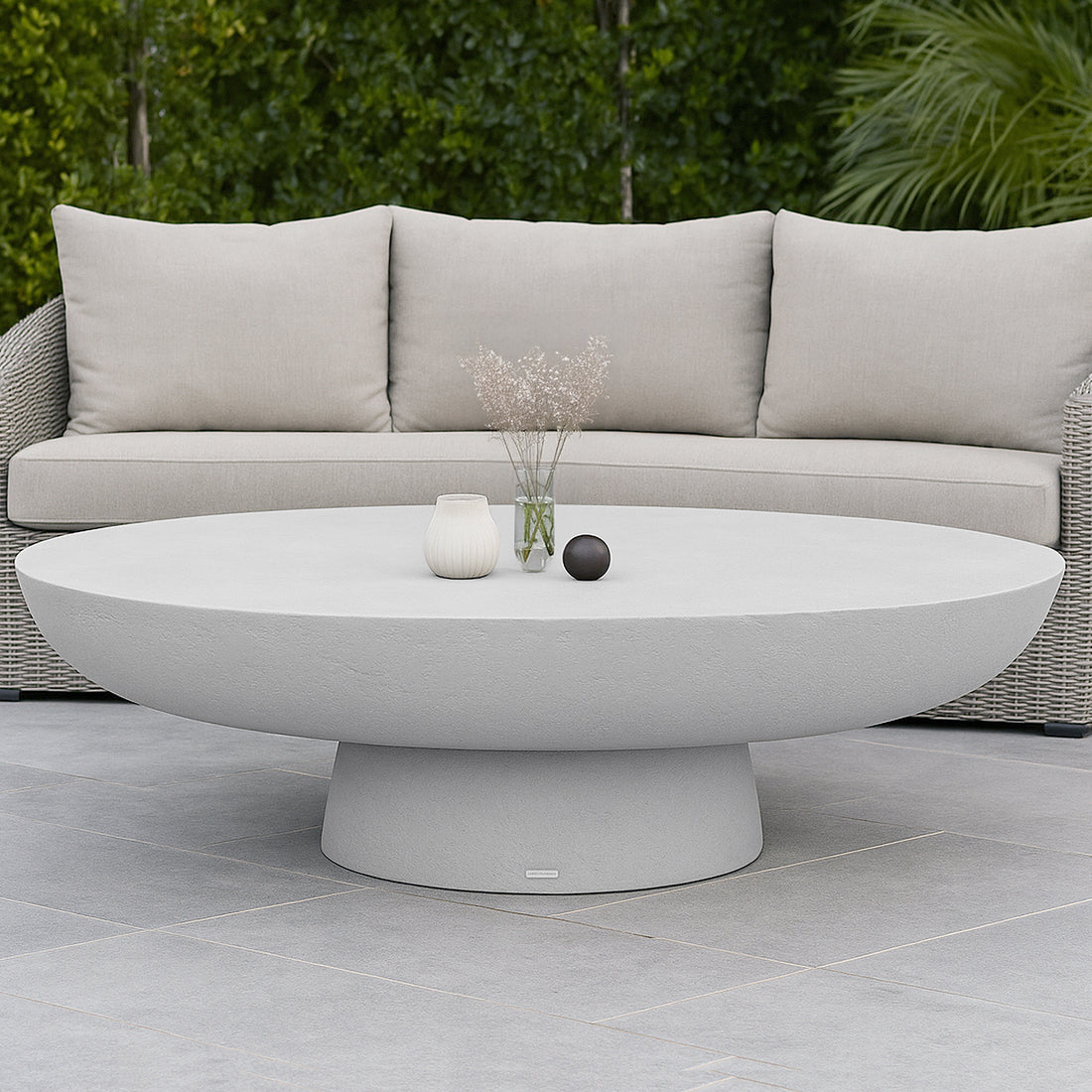 Cassius Oval Outdoor Concrete Coffee Table in White with smooth oval top and sculptural base, styled with white vase, glass