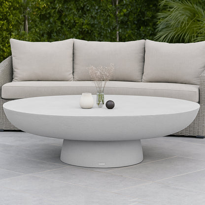 Cassius Oval Outdoor Concrete Coffee Table in White with smooth oval top and sculptural base, styled with white vase, glass