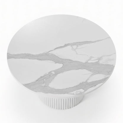 Close-up of a round dining table featuring a white stone top with grey marble veining and a white fluted pedestal base_3