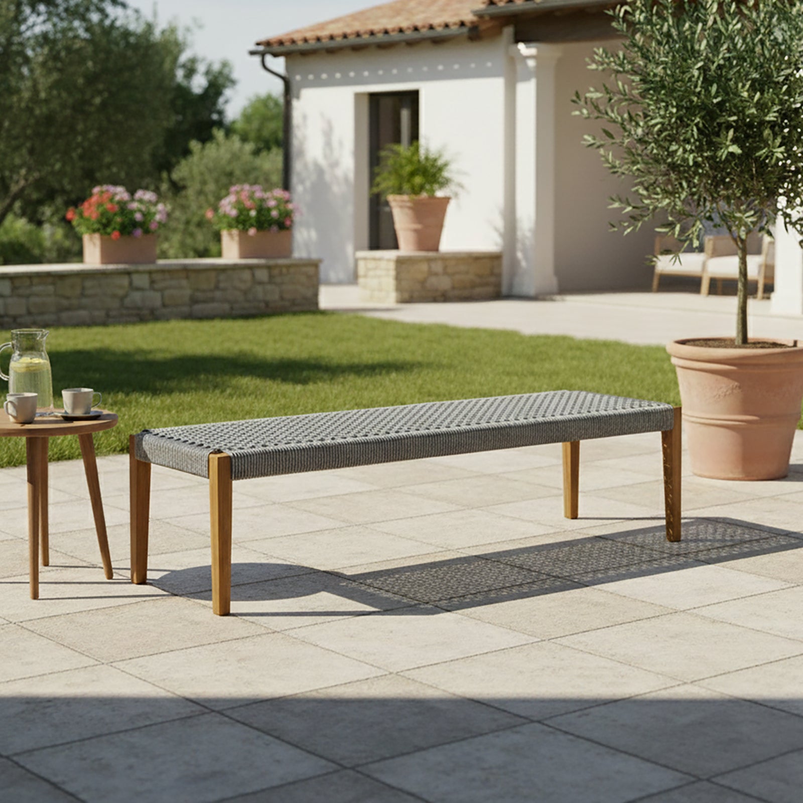 Fentan 4 Seater Acacia Hardwood Outdoor Bench in Light Grey, features a woven seat and wooden legs, set in a garden patio with a side table holding a pitcher and cups.
