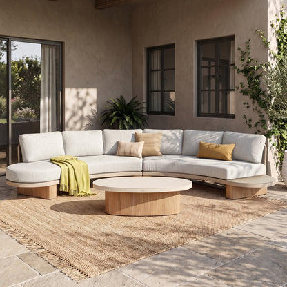 Sectional sofa and round wooden coffee table styled in a bright modern outdoor or patio setting.