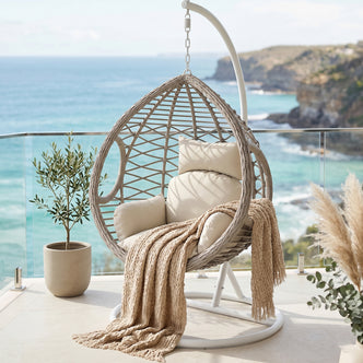 Hilda Large Outdoor Hanging Egg Chair in Sage, teardrop-shaped woven seat with cream cushions and beige throw, suspended from
