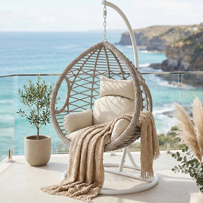 Hilda Large Outdoor Hanging Egg Chair in Sage, teardrop-shaped woven seat with cream cushions and beige throw, suspended from