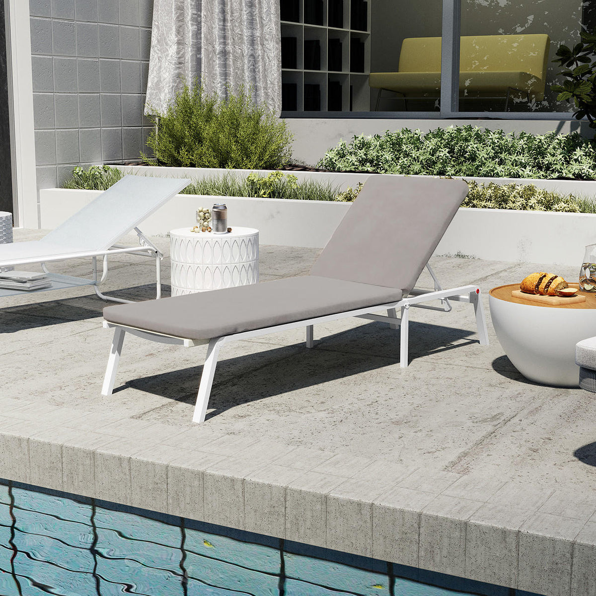Jabari Outdoor Sun Lounger with Cushion in Warm Grey rests poolside on a concrete deck, with a white frame and pale gray cushion, surrounded by snacks and greenery for a luxurious lounging experience.