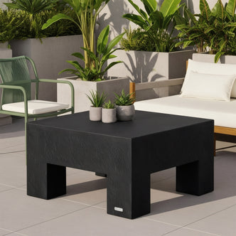 Maxon Square Outdoor Concrete Coffee Table in Black with block legs, styled on a tiled patio with outdoor sofa and plants