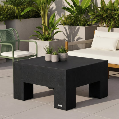Maxon Square Outdoor Concrete Coffee Table in Black with block legs, styled on a tiled patio with outdoor sofa and plants