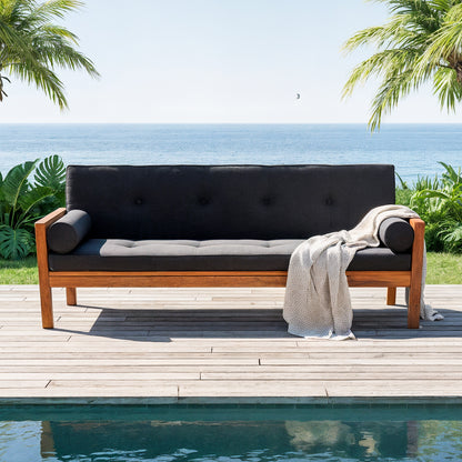Luxo Meves Hardwood Outdoor Daybed Sofa & Cushion in Black, featuring a wooden frame with dark gray cushions and bolster pillows, set on a deck beside a pool with tropical ocean view.