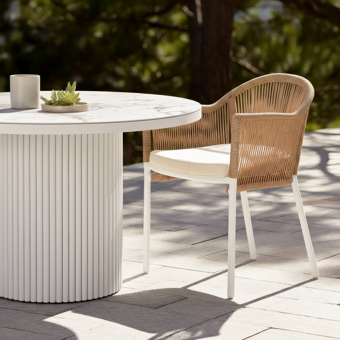 Mindanao PE Wicker Outdoor Dining Chair in Natural with beige cushion and white legs, shown beside a white fluted outdoor