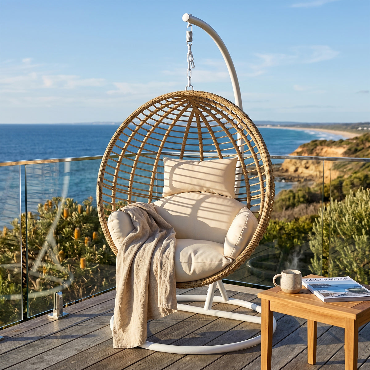Napili Outdoor Hanging Egg Chair with woven rattan shell, cream cushions, white metal frame, coastal balcony setting