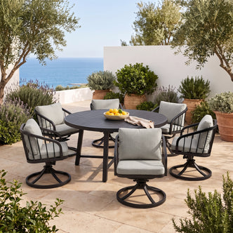 Outdoor dining set with round table and six chairs on a tiled patio with greenery and ocean view