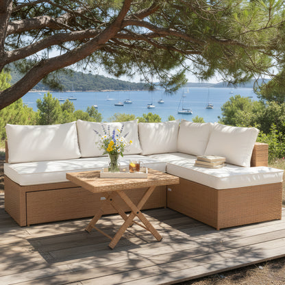 L-shaped outdoor wicker lounge set with white cushions and a square wicker coffee table on a wooden deck overlooking the ocean.