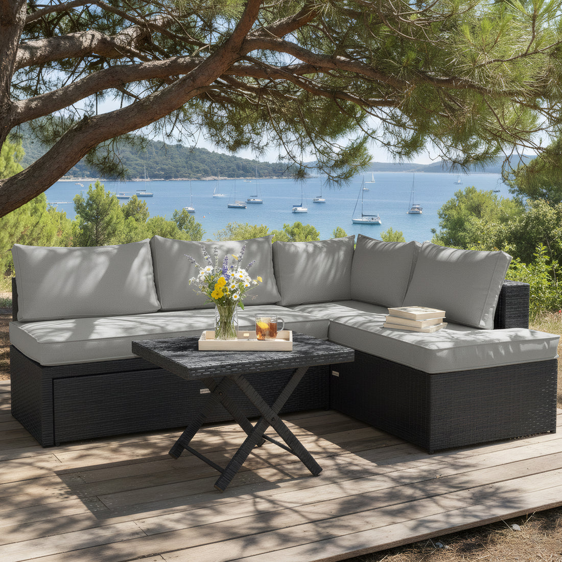 4 Seater Rattan Outdoor Corner Sofa Set in Warm Grey. L-shaped black wicker outdoor lounge set with grey cushions and a matching square wicker coffee table on a wooden deck.