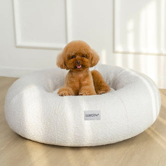 Kyra Medium Boucle Pet Bed – Light Beige Comfort: close-up of a dog lounging in a plush, supportive boucle pet bed with raised bolsters, featuring a visible white label with black text.