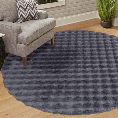 Armida 160cm Round Fluffy Faux Fur Bubble Rug in Grey with a shaggy bubble texture, partially covered by a light gray upholstered armchair and chevron-patterned pillow, set on a wooden floor.
