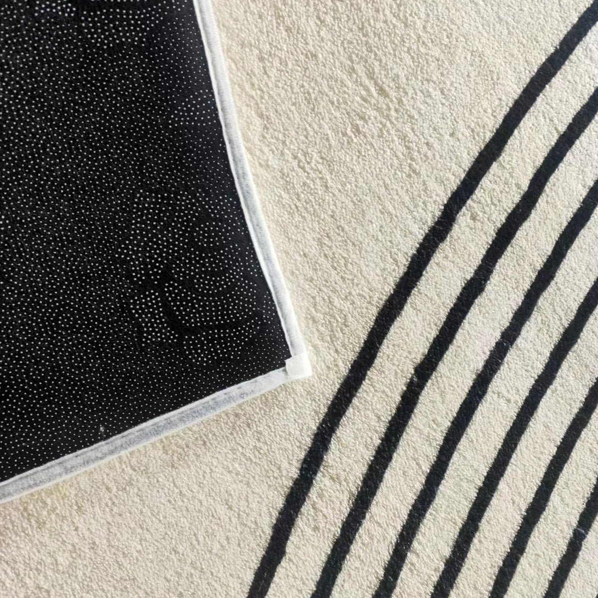 Close-up of Axland Modern Abstract Rug 160x230cm, showing a cream pile with bold black stripes overlapping a dotted, black anti-slip rug pad on the left.