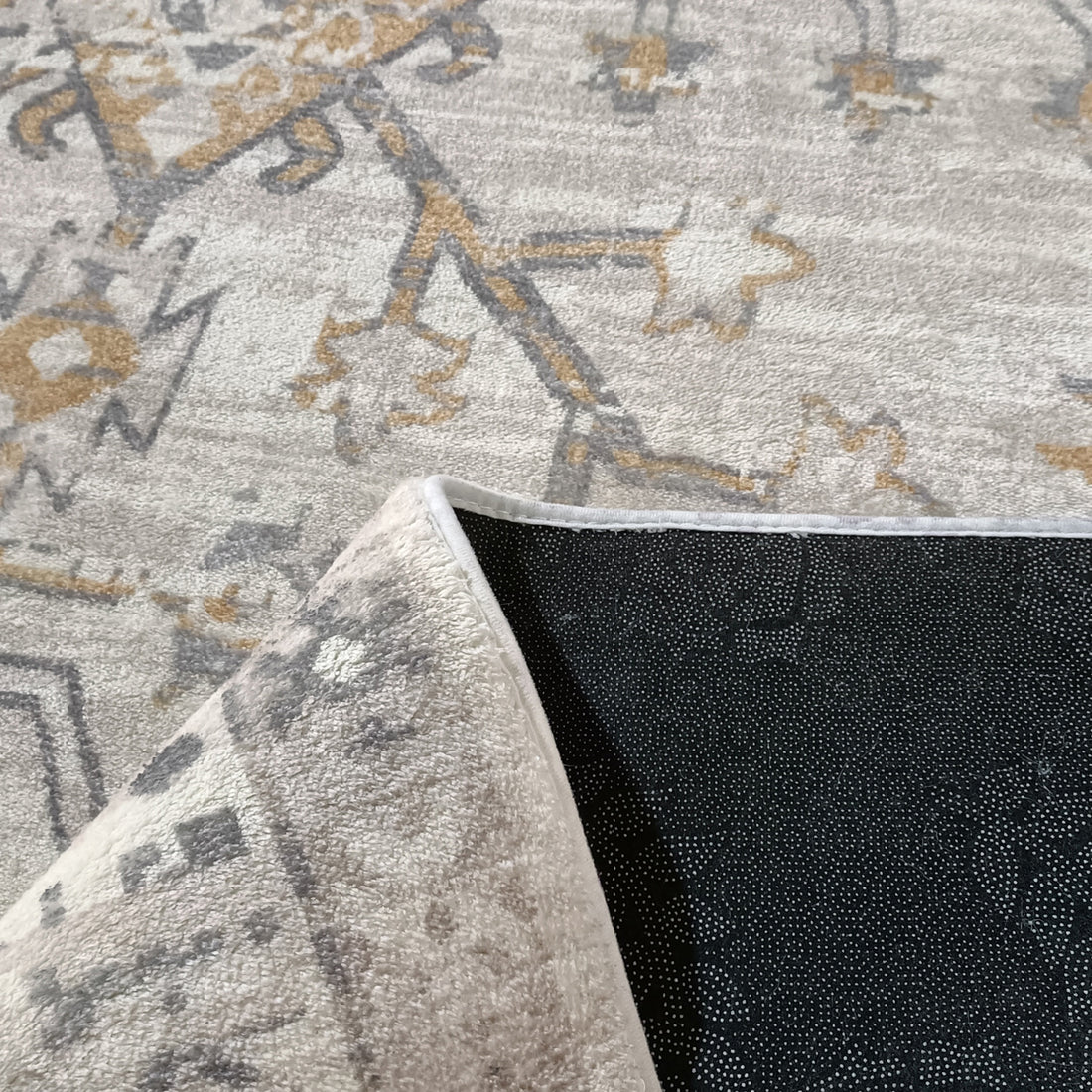 Bortan Persian Indoor Rug 160x230cm with cream and gray abstract motifs, shown with a corner peeled back revealing its black non-skid backing with white grip points.