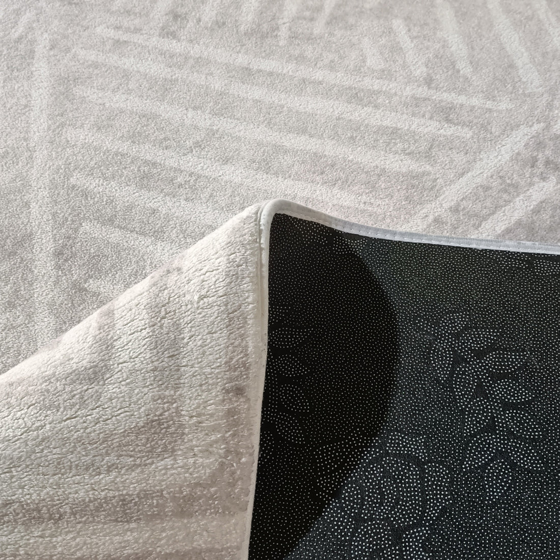 Close-up of Duved floor rug corner showing white textured pile and black dotted non-slip backing with bound edge